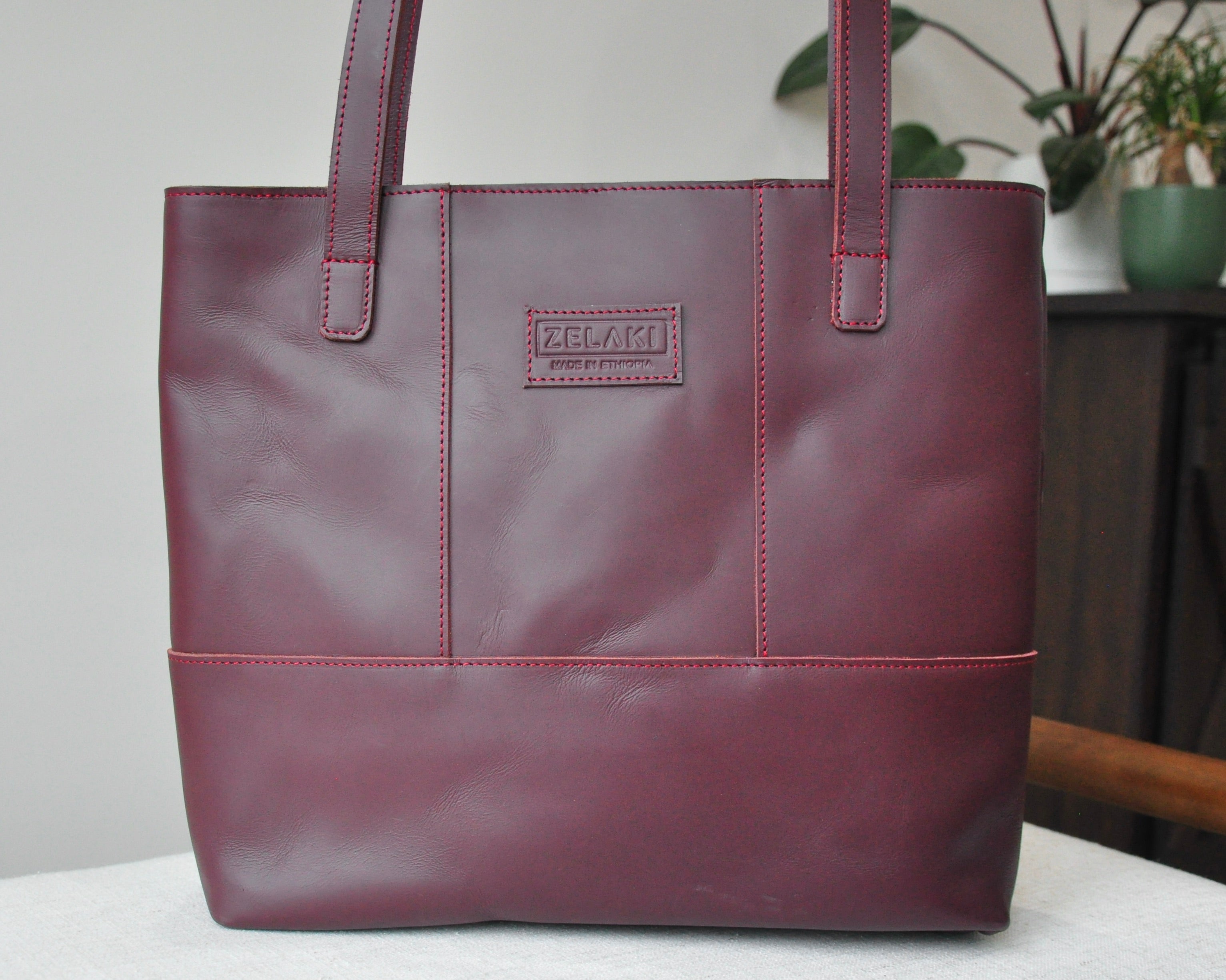Large full-grain leather tote bag with minimalist design, featuring a zipper closure and an inside pocket in burgundy