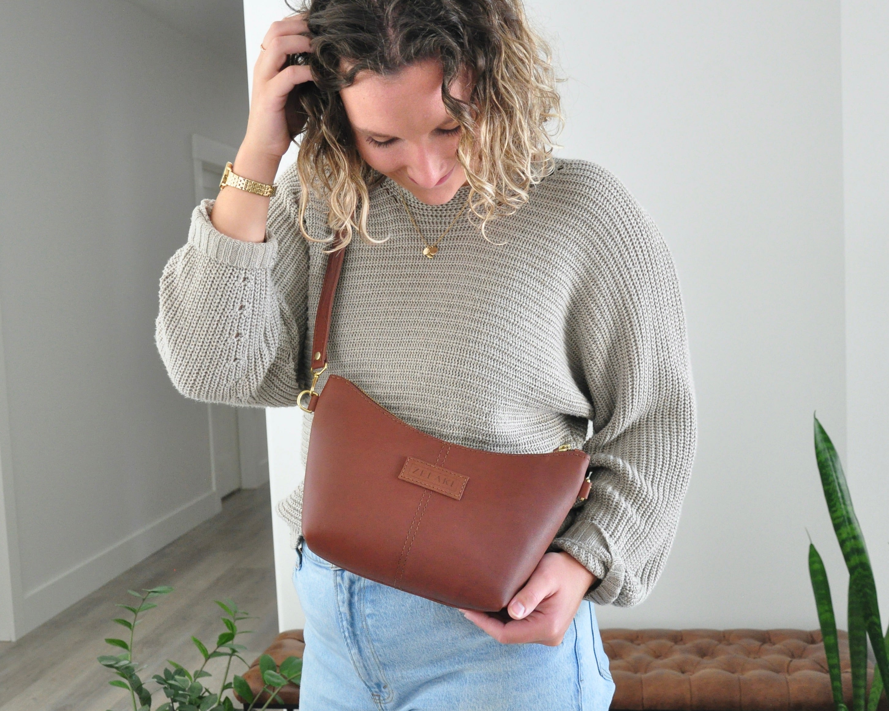 Woman holding a brown leather bag indoors with a neutral background