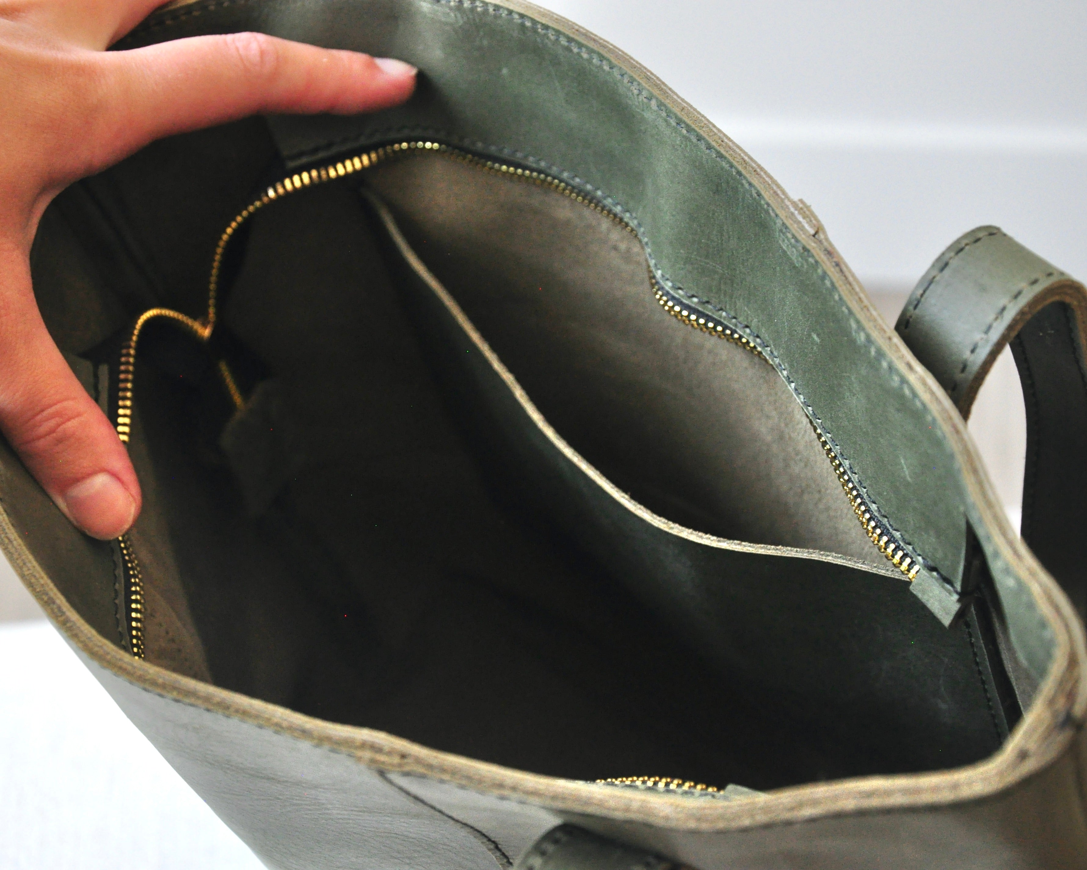 Large full-grain leather tote bag with minimalist design, featuring a zipper closure and an inside pocket in olive green