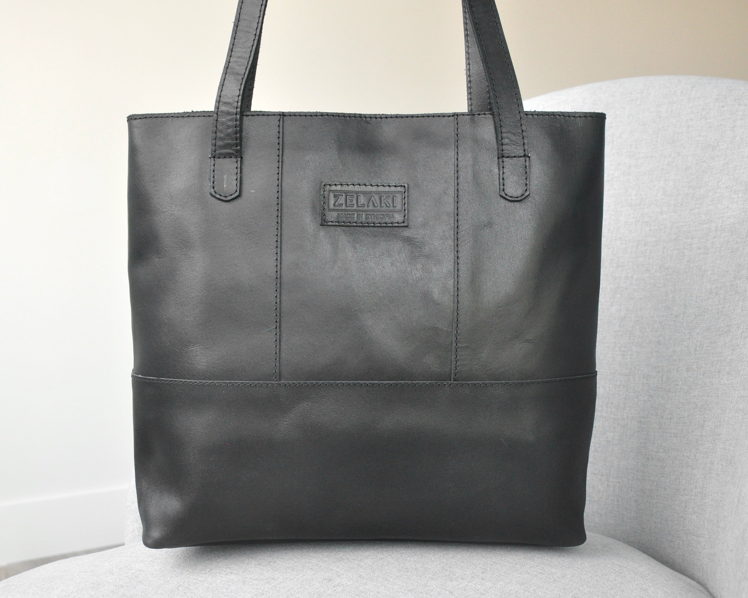 Large full-grain leather tote bag with minimalist design, featuring a zipper closure and an inside pocket in black