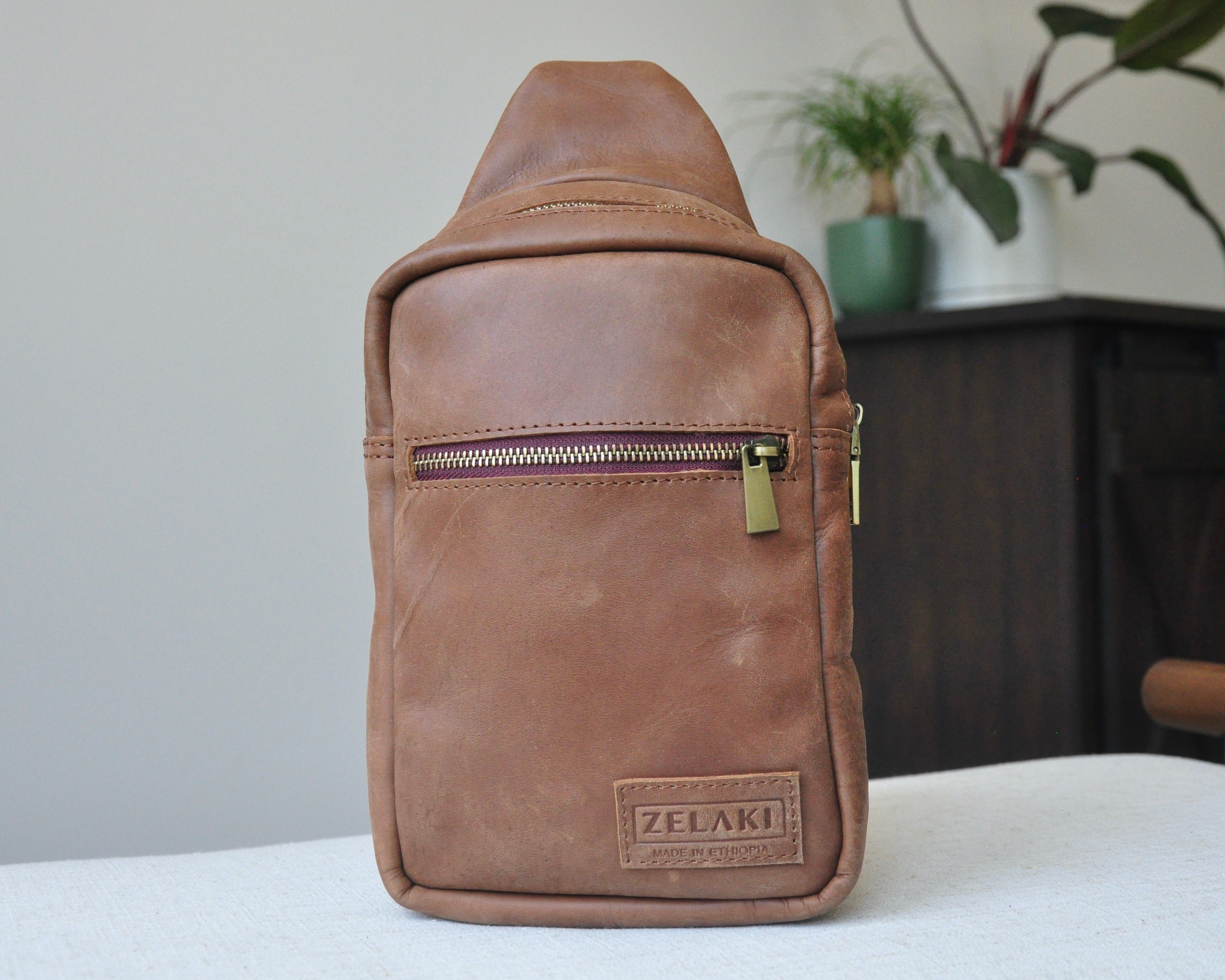 Full-grain Leather sling bag with multiple pockets, designed for versatile wear as a crossbody on your front or back, small to medium size in brown