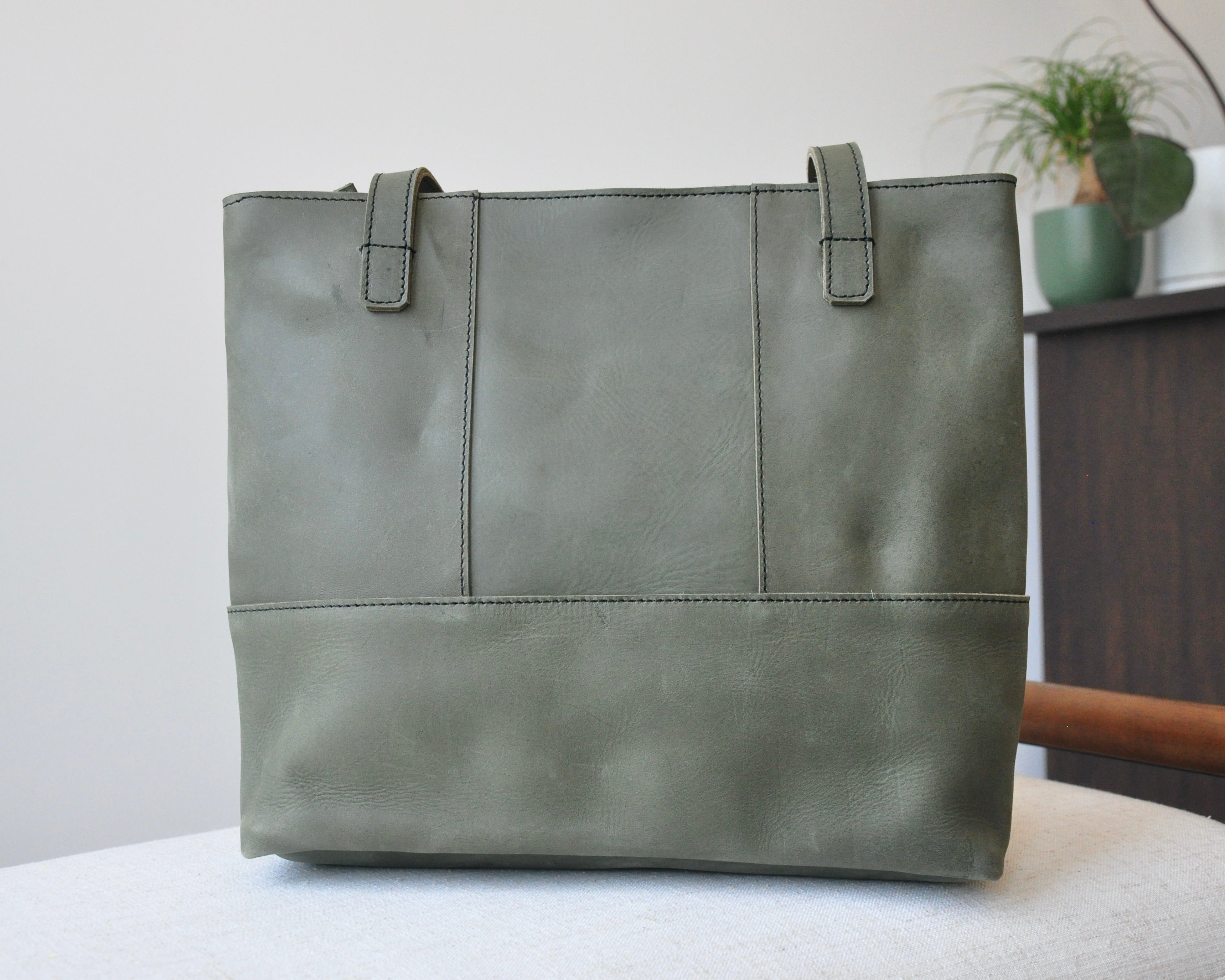 Large full-grain leather tote bag with minimalist design, featuring a zipper closure and an inside pocket in olive green