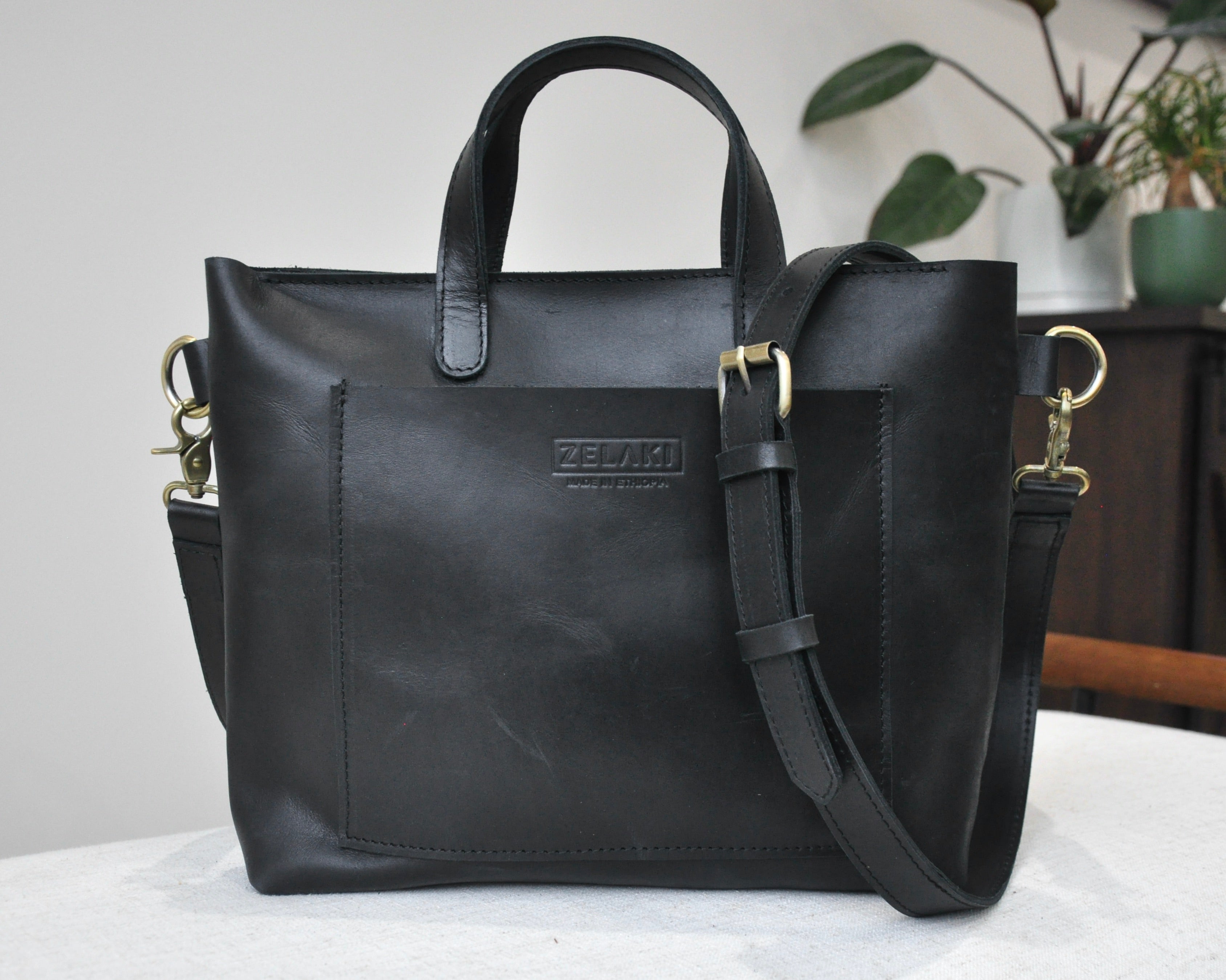 A medium sized, black leather tote bag with a sleek, minimalist design featuring a top handle and adjustable crossbody strap