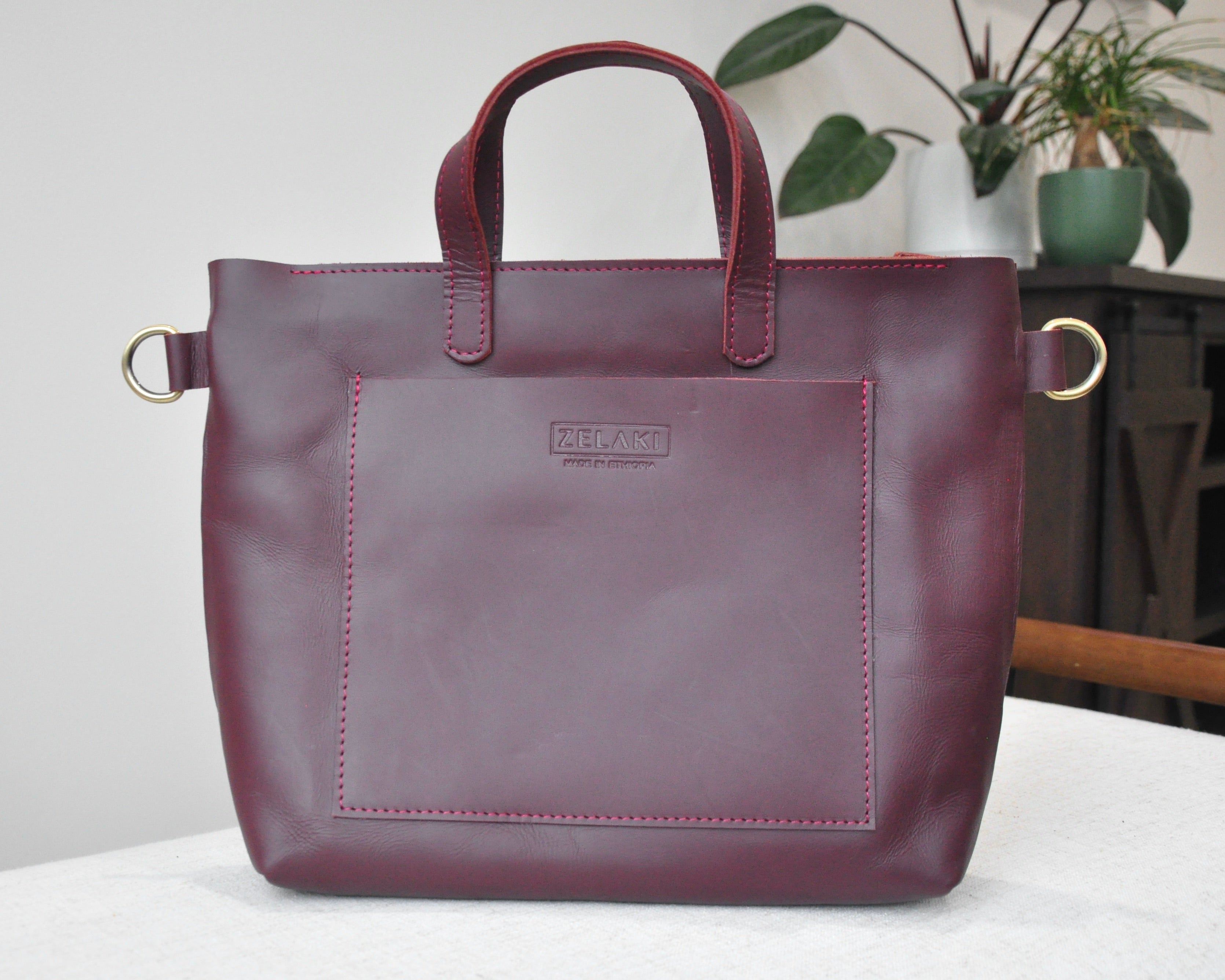 A medium sized, burgundy leather tote bag with a pockets, zipper closure, and adjustable crossbody strap