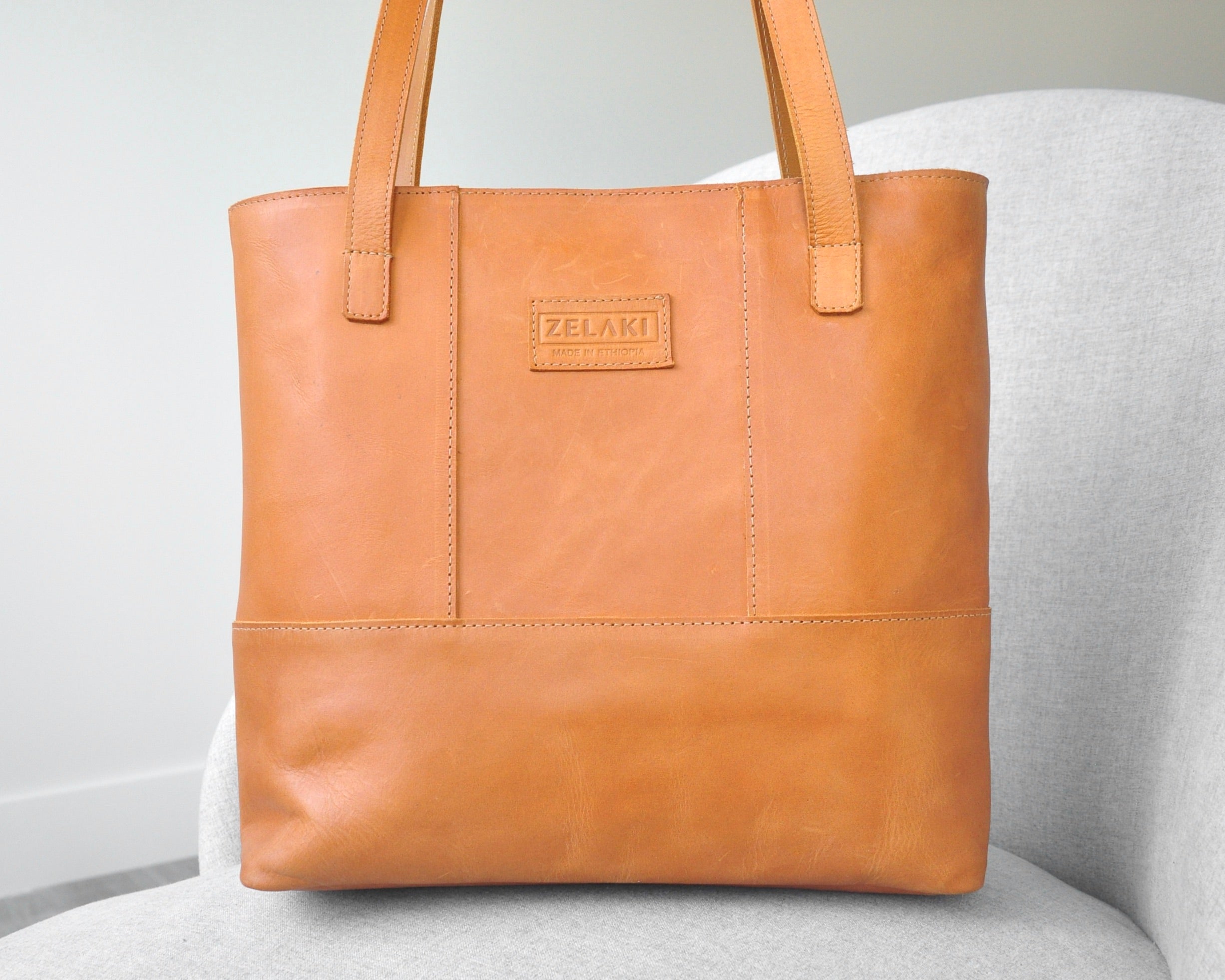 Large full-grain leather tote bag with minimalist design, featuring a zipper closure and an inside pocket in tan