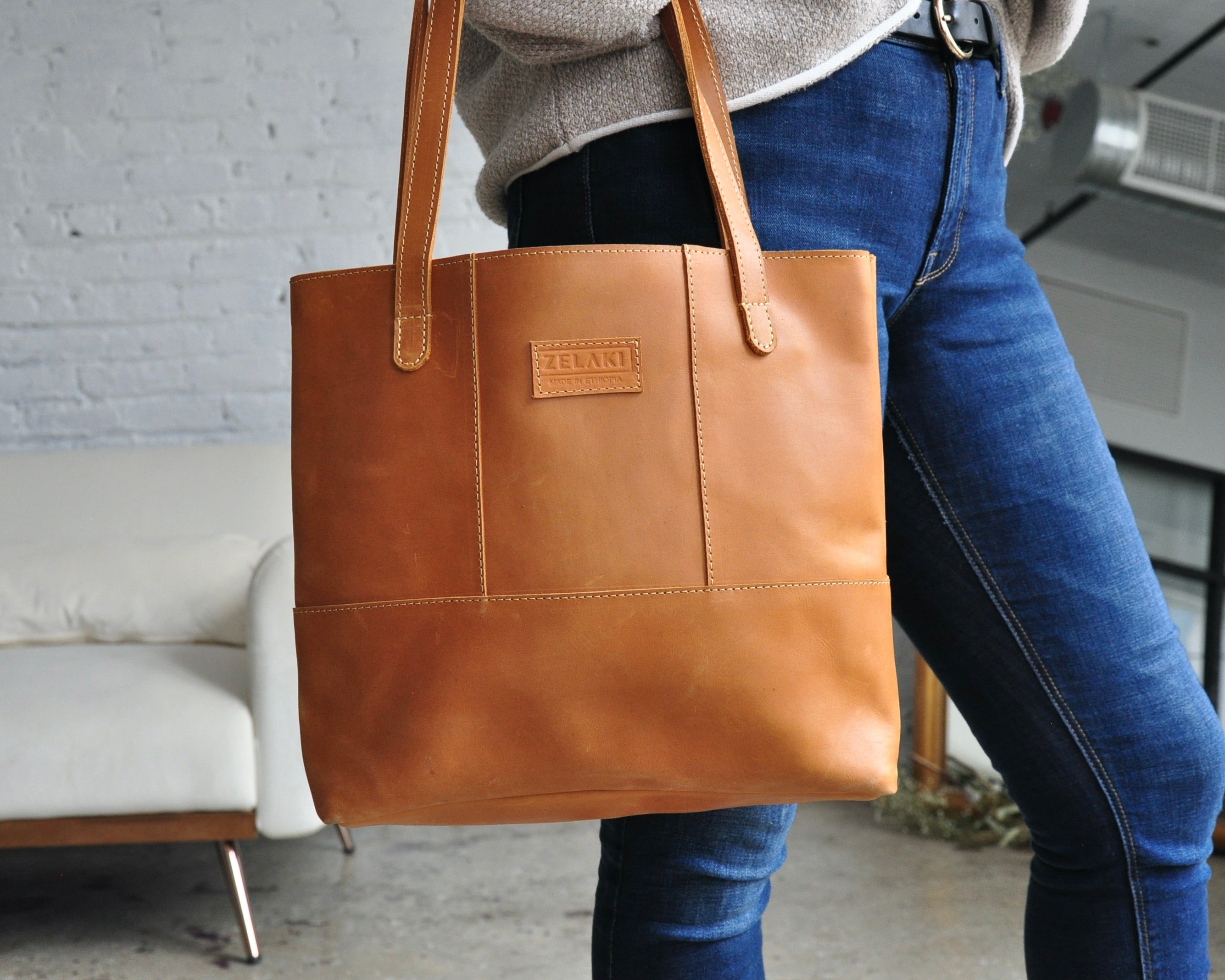 Large full-grain leather tote bag with minimalist design, featuring a zipper closure and an inside pocket in tan