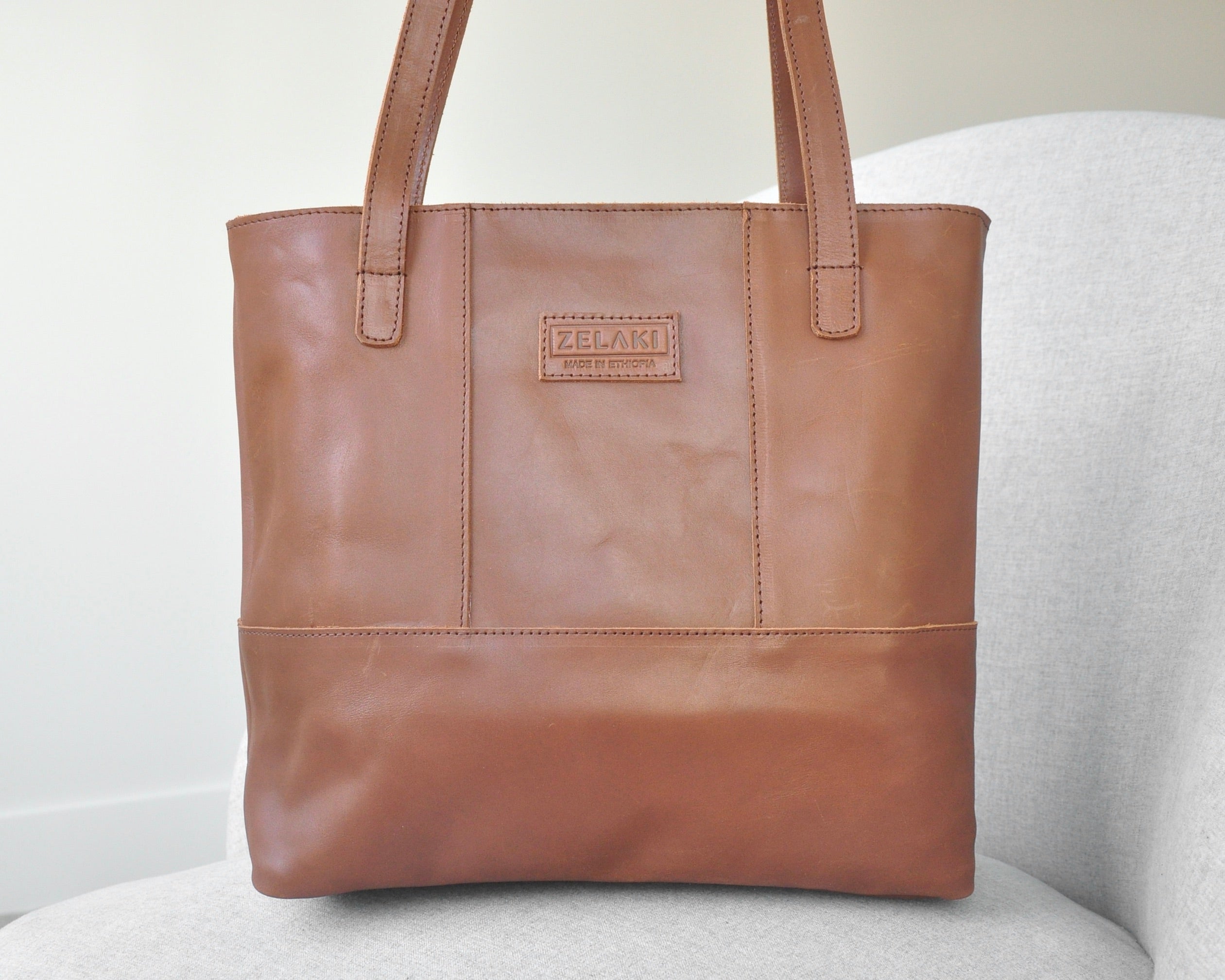 Large full-grain leather tote bag with minimalist design, featuring a zipper closure and an inside pocket in medium brown