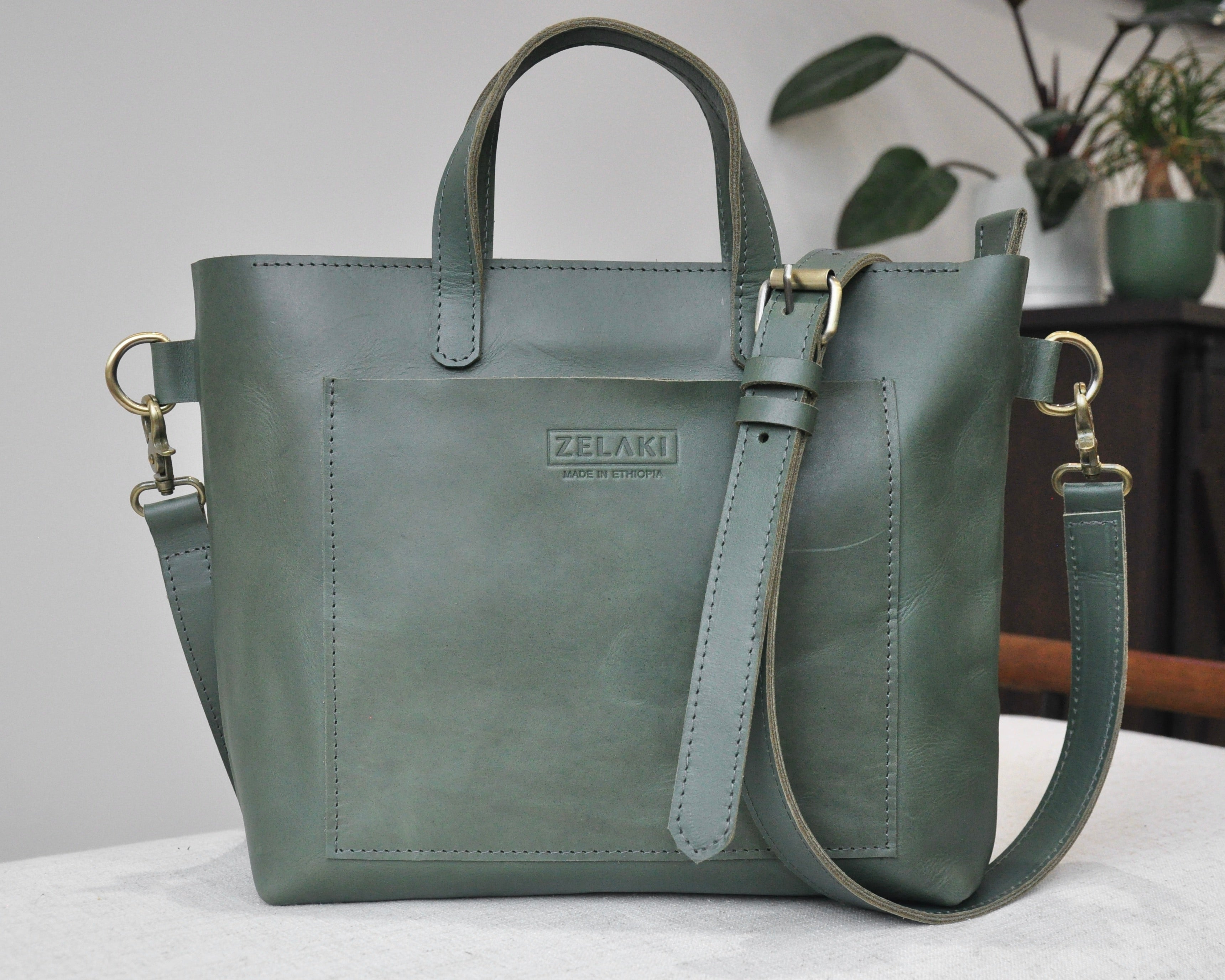A medium sized, olive leather tote bag with a sleek, minimalist design featuring a top handle and adjustable crossbody strap