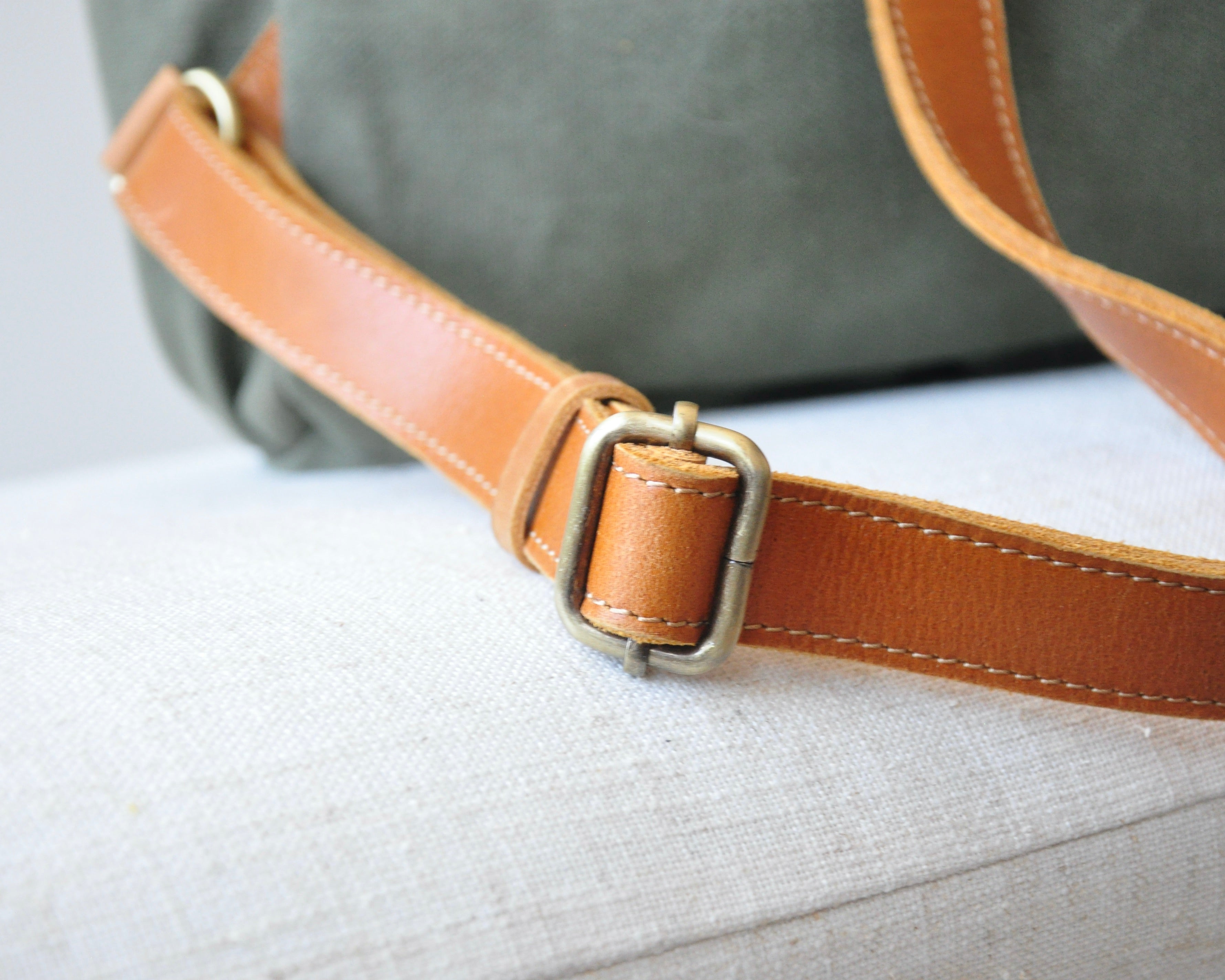 An olive green canvas backpack with full-grain leather accents, featuring two shoulder straps, and top handles.