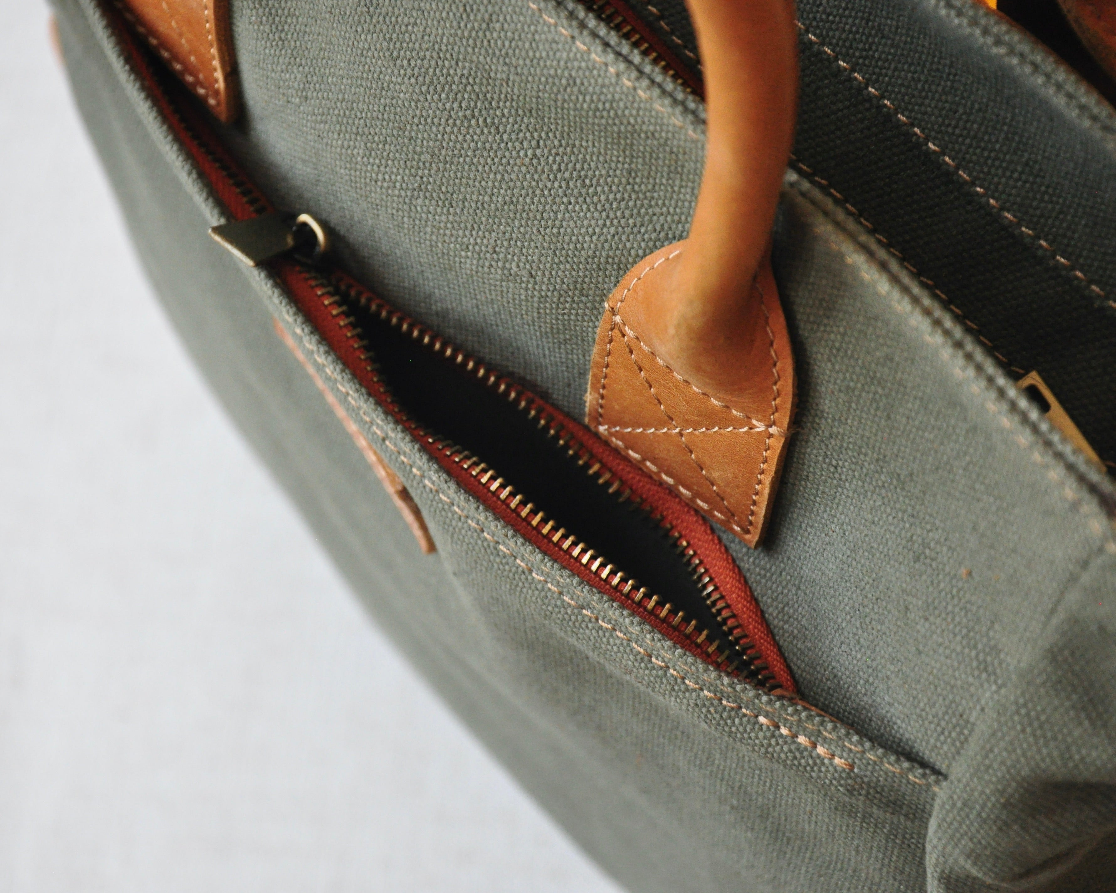 An olive green canvas backpack with full-grain leather accents, featuring two shoulder straps, and top handles.