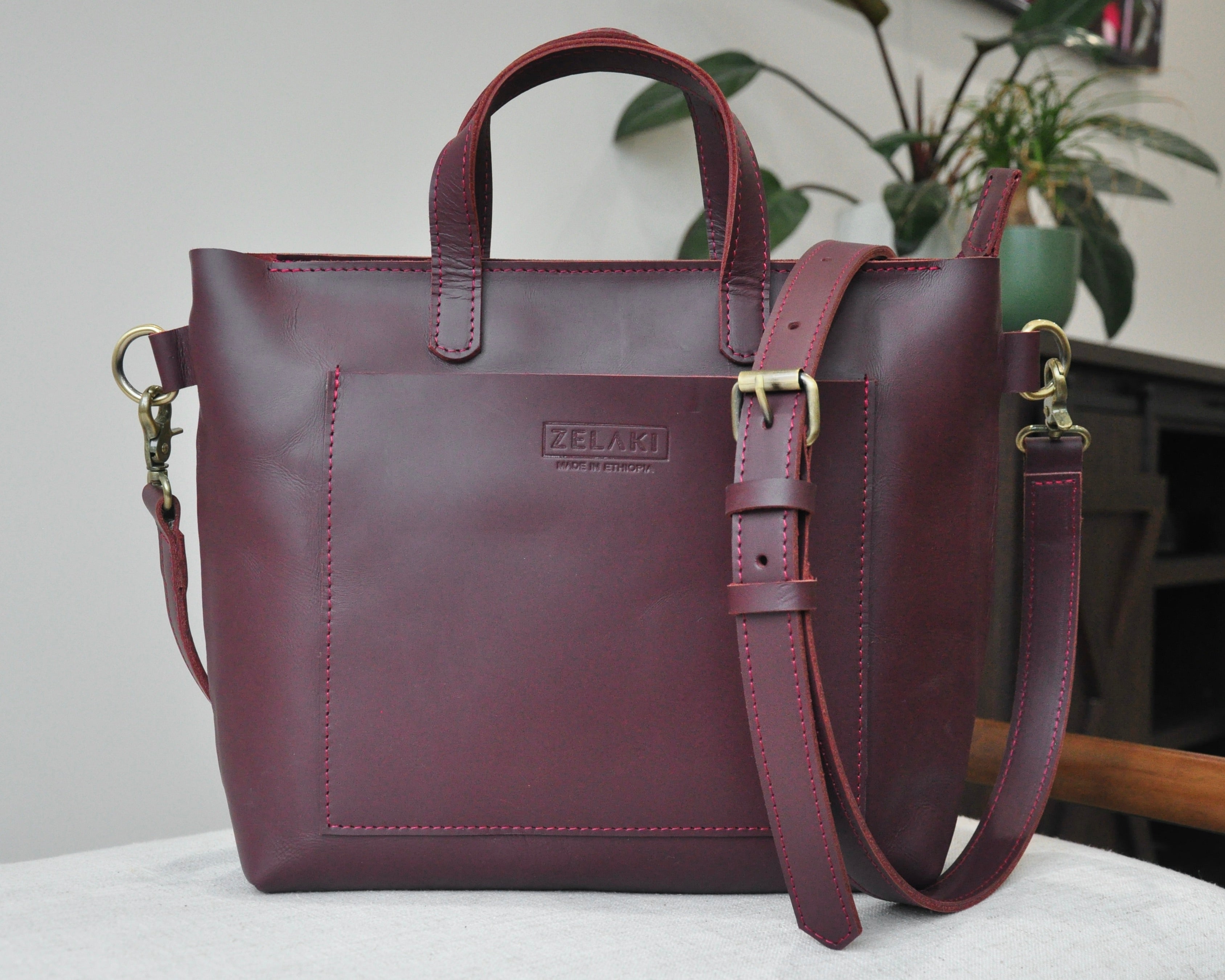 A medium sized, burgundy leather tote bag with a sleek, minimalist design featuring a top handle and adjustable crossbody strap