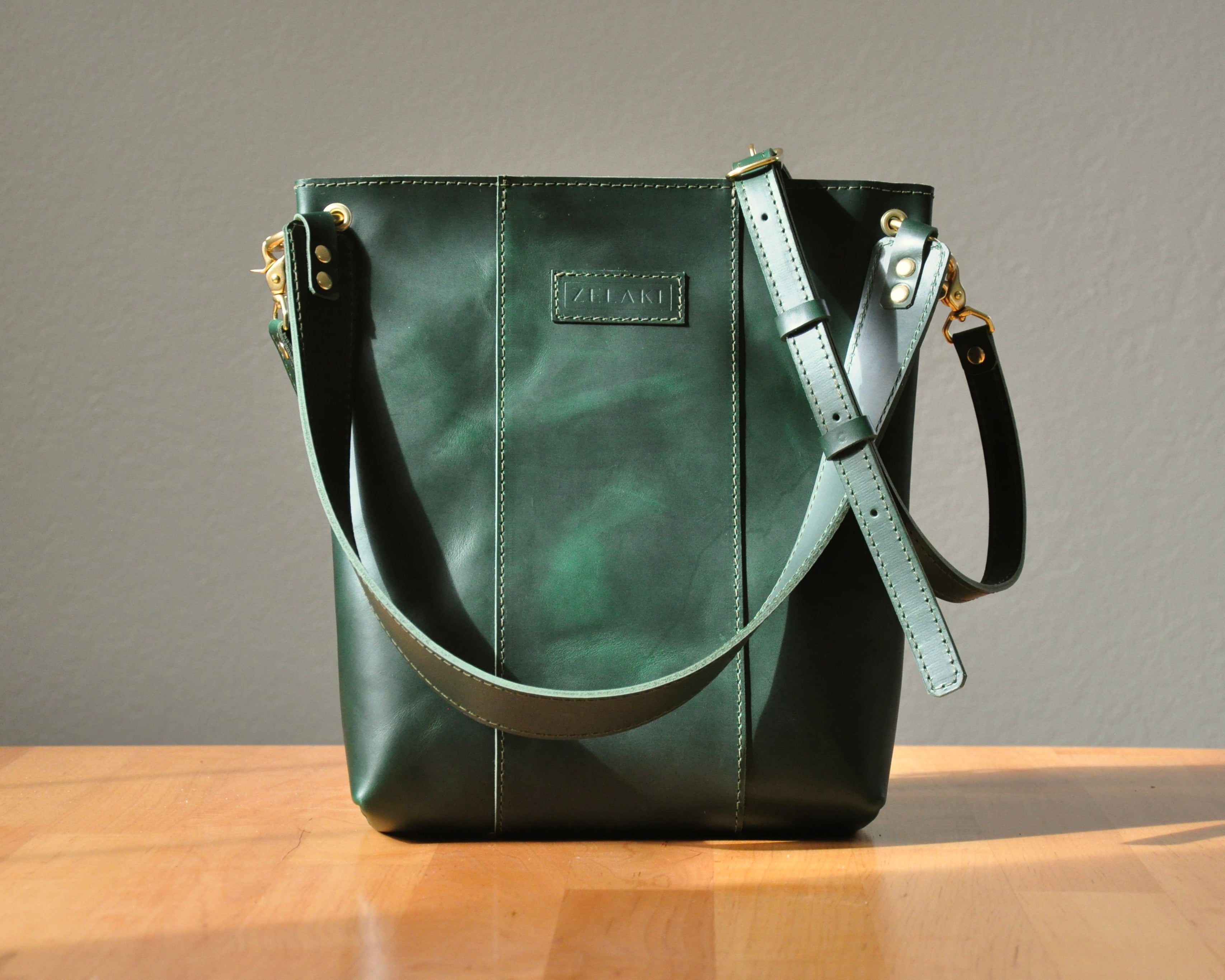 Green leather handbag with a strap on a wooden surface and gray background